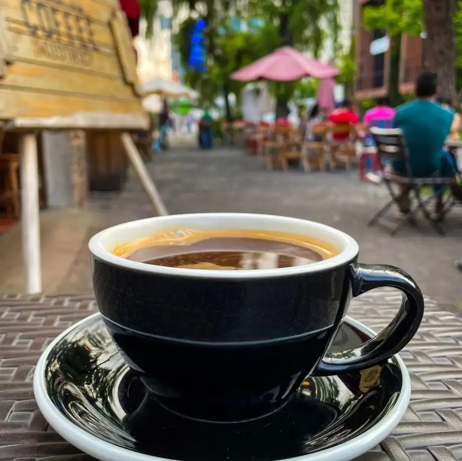 Taza negra de café americano sobre una mesa en la calle peatonal de 4 Grados Norte