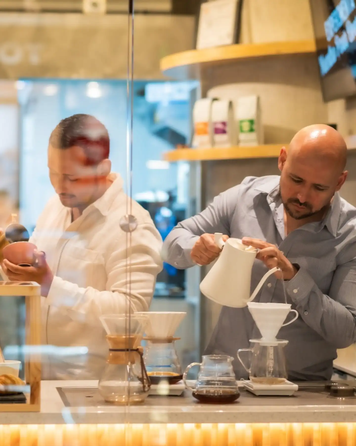 Barista sirviendo café en filtro de cerámica frente a otra persona que prepara un pour over