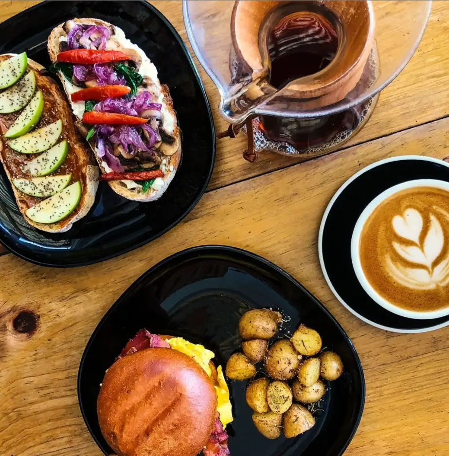 Mesa con tostadas de vegetales, hamburguesa con papas, latte y Chemex