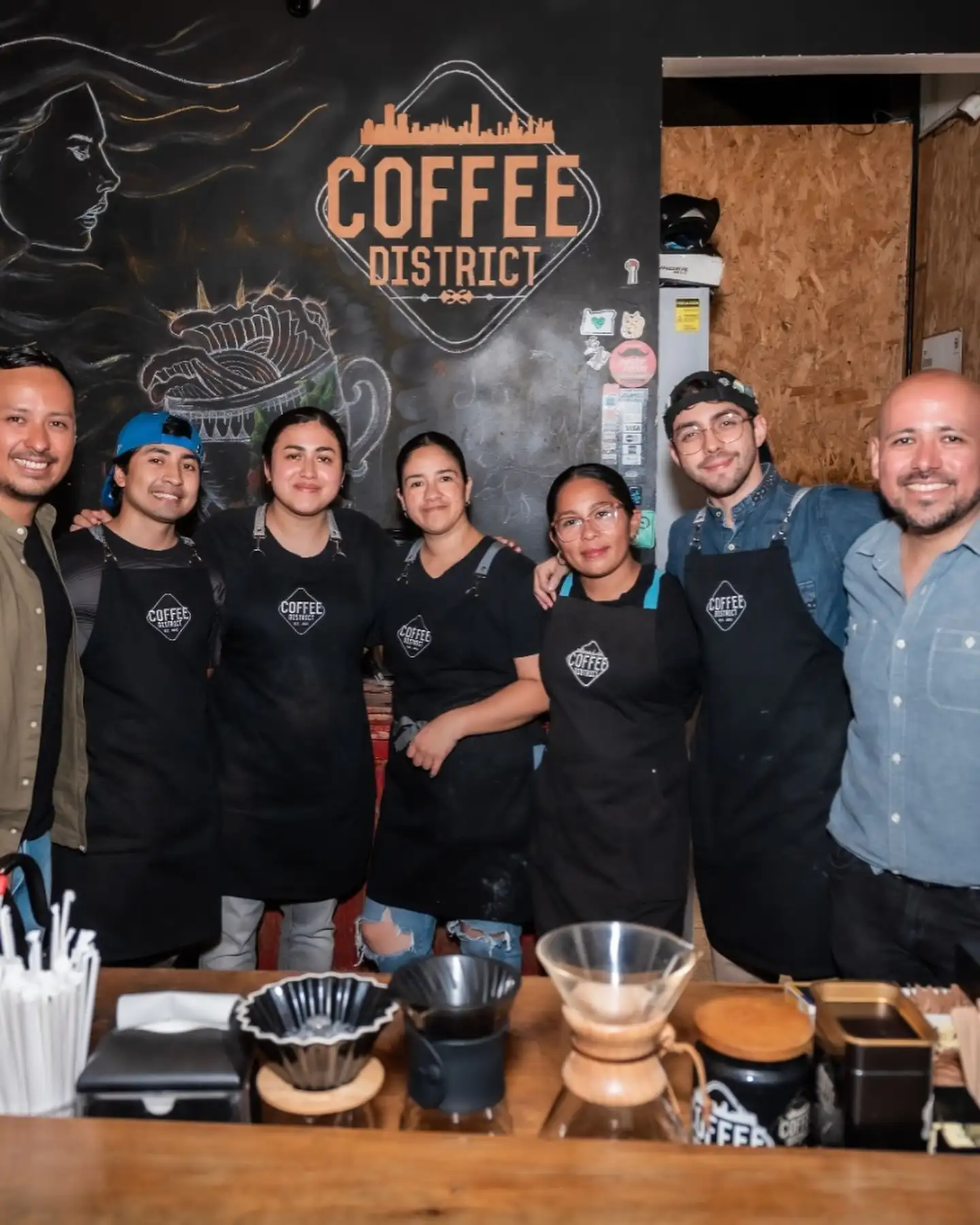 Equipo de Coffee District frente a la barra con Chemex y filtros sobre el mostrador