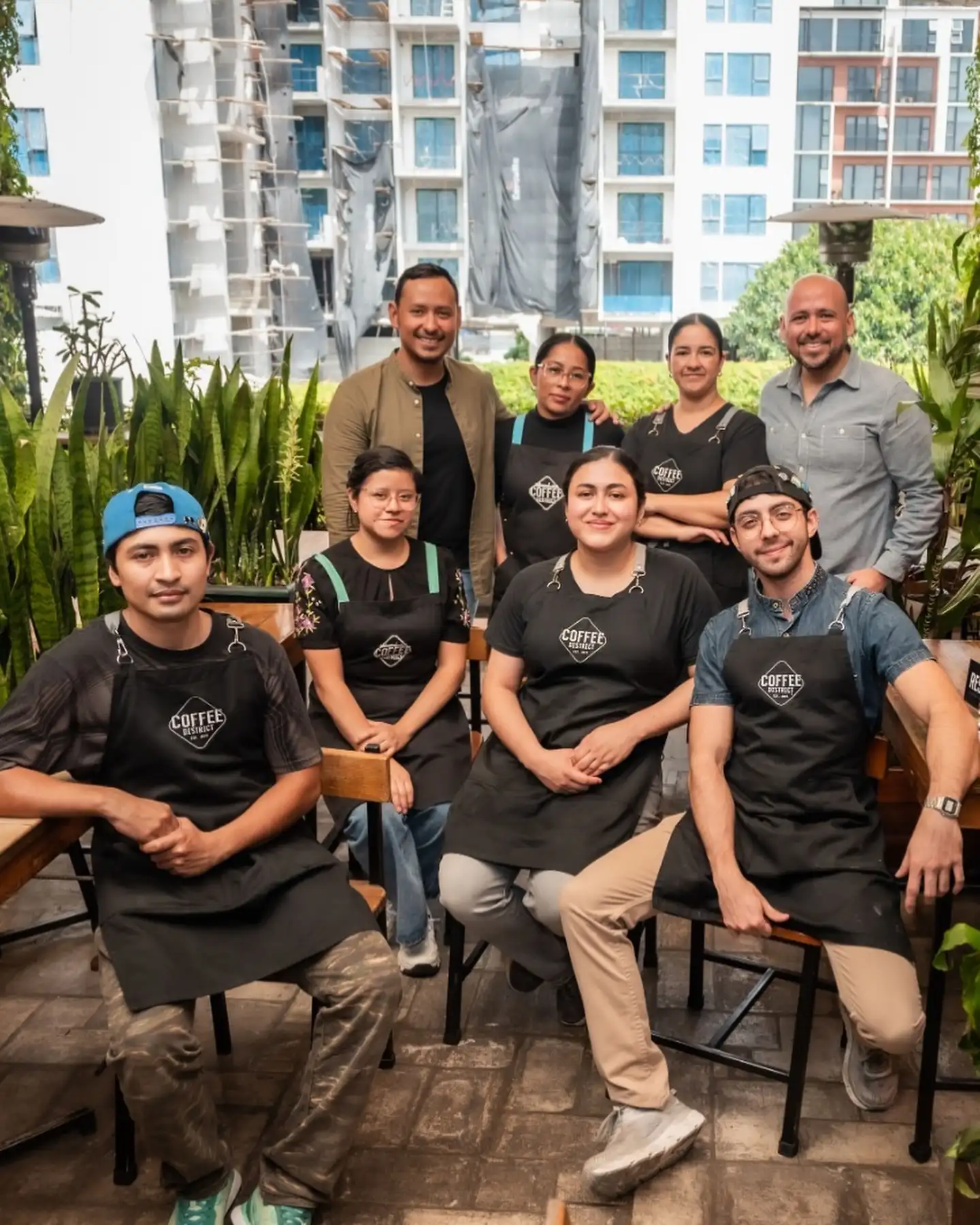 Equipo de baristas y cocina de Coffee District posando en la terraza entre plantas