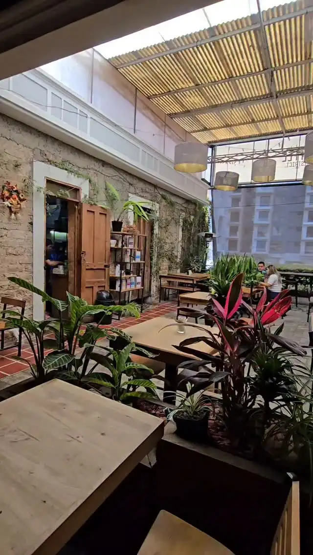 Patio interior de la Casa del Águila con muros de piedra, puertas de madera, plantas y mesas